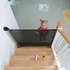 A baby gate is installed at the top of a wooden staircase, with a toddler looking up at the camera. Náhľad obrázku produktu