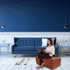 A woman using a laptop while sitting on a folded mattress in a living room. Podgląd zdjęcia produktu