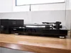 A black turntable and amplifier sit on a wooden surface. Produktbild-Vorschau