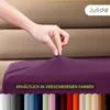 A hand is shown stretching a purple fitted sheet, with a row of different colored sheets shown at the bottom. Produktbild-Vorschau