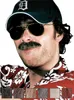 A man wearing a baseball cap and sunglasses, with a mustache, and a Hawaiian shirt. Produktbild-Vorschau