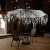 An outdoor patio at night with an umbrella decorated with icicle lights, a table, and chairs. Produktbild-Vorschau