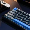 A close-up view of a mechanical gaming keyboard with blue and gray keycaps, illuminated by blue LED lighting. Produktbild-Vorschau