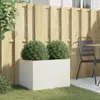 A white rectangular planter with two green bushes sits on a grassy lawn in front of a wooden fence. A black metal chair and table are visible to the right. Anteprima dell’immagine prodotto
