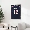 A framed sports jersey is displayed on a wall in a living room setting, next to a chair and a side table. Náhled obrázku produktu