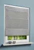 A gray striped Roman blind is installed on a window, with a view of trees and foliage visible through the lower part of the window. Two small decorative candle holders are placed on the windowsill. Produktbild-Vorschau