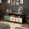 A TV stand with decorative drawers is placed in a room with a bed in the foreground and framed pictures on the wall. Podgląd zdjęcia produktu