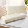 Two pillows are displayed on a white surface, with a wooden headboard and a plant in the background. Produktbild-Vorschau