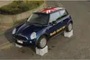 A blue Mini Cooper car with a Union Jack on the roof is parked on a street, with its wheels resting on four clear plastic storage boxes. Náhled obrázku produktu