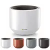 A large white planter pot with a dark interior is shown from the front, with smaller versions of the pot in white, copper, gray, and dark gray displayed below. The product has a logo and text on its front. Produktbild-Vorschau