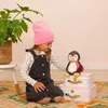 A young girl in a pink beanie and denim overalls is playing with a stuffed penguin toy next to two white suitcases. Anteprima dell’immagine prodotto