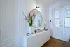 A bright and airy entryway with a white console table, a round mirror, and a vase of flowers. Anteprima dell’immagine prodotto