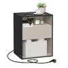 A black and beige nightstand with a drawer and a storage box, featuring a plant, a cup of coffee, and a phone on top. A power cord is visible at the bottom. Produktbild-Vorschau