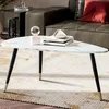 A triangular coffee table with a marble-like top and black legs with gold accents, placed on a rug in a living room setting. Voir les images du produit