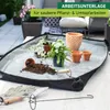 A gardening mat with plants, pots, and tools on a table, with a blurred background of a patio. Produktbild-Vorschau