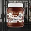 A jar of OstroVit Creametto Chocolate protein spread is displayed in front of gym equipment. Produktbild-Vorschau