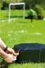 A person is locking a black box in a grassy yard with a soccer goal and a child in the background. Anteprima dell’immagine prodotto