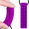 A hand is holding a purple teething toy shaped like a Lego brick. Produktbild-Vorschau