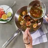 A person is using a ladle to pour sauce from a small pan into a larger frying pan containing scallops. Náhled obrázku produktu