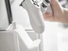 A hand holding a white game controller over a white controller stand. Produktbild-Vorschau