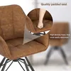 Close-up of a brown upholstered chair with a hand pressing into the seat, highlighting its padding. Another chair is blurred in the background. Produktbild-Vorschau