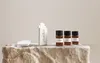 Three small amber bottles with black caps and labels, a white packaging box with text, and two white rectangular objects are arranged on a textured, light-colored stone surface against a plain, light-colored background. Náhled obrázku produktu
