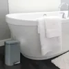 A bathroom scene with a bathtub, towels, and a trash can. Anteprima dell’immagine prodotto