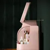 A pink cosmetic organizer with a mirror lid open, showing various bottles and containers inside. The background is a dark green textured curtain. Anteprima dell’immagine prodotto