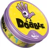 A round tin can for the board game Dobble (Spot It!). The tin is purple and yellow with various cartoonish icons and the game's logo. Voir les images du produit