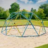 A blue and yellow geodesic dome climber sits on a sand-covered playground area, with a grassy park and trees in the background. Náhled obrázku produktu