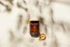 A WoodWick candle with incense and myrrh is placed on a light-colored surface, with shadows of leaves cast on it. Voir les images du produit