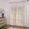 A sheer curtain with a subtle pattern hangs in front of a window, with a vintage-style dresser and a vase of flowers to the left. Produktbild-Vorschau