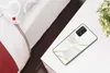 A smartphone case with an abstract pattern is placed on a white surface next to a bed and a plant. Produktbild-Vorschau