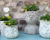 Three planters with yellow flowers are arranged in front of a brick wall. Voir les images du produit