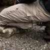 A person is kneeling on rocks and gravel, wearing beige outdoor pants and brown boots. Náhľad obrázku produktu