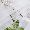 A close-up view of a white sheer curtain with embroidered brown floral patterns and a printed image of green apples underneath. Produktbild-Vorschau