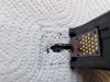 A close-up of a printer ink cartridge nozzle being wiped on a paper towel, showing black ink residue. Produktbild-Vorschau