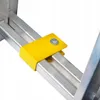 A close-up view of a yellow metal bracket attached to an aluminum ladder rail with a bolt. Produktbild-Vorschau