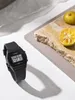 A black Casio digital watch is placed on a white surface, with a shadow cast to the side. In the background, a rough stone slab holds two halves of a sliced orange. Anteprima dell’immagine prodotto