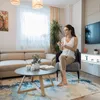 A woman is sitting in a chair in a living room, holding a cup. Náhled obrázku produktu