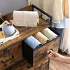 A hand is opening a drawer of a rustic-style dresser, revealing folded clothes. A handbag and decorative items are on top of the dresser. Náhled obrázku produktu