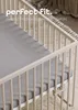 A close-up view of a crib with a gray fitted sheet. Produktbild-Vorschau