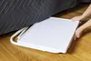 A person's hands are placing a white tray under a bed. Anteprima dell’immagine prodotto