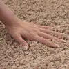 A hand is shown resting on a beige shaggy carpet. Podgląd zdjęcia produktu