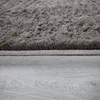 A close-up view of a fluffy gray rug with a textured border, resting on a gray wooden floor. Produktbild-Vorschau