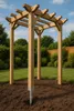 A wooden pergola structure is installed in a garden setting with grass and bushes in the background. Produktbild-Vorschau