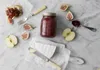 A still life arrangement of food items including a jar of jam, figs, apples, and cheese, set on a marble surface. Voir les images du produit