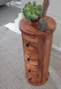 A round wooden side table with four drawers sits on a textured rug next to a wall. A succulent plant and a decorative feather are on top of the table. Produktbild-Vorschau