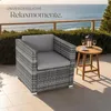 An outdoor seating area with a rattan armchair and a small wooden table next to the sea. Produktbild-Vorschau