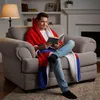 A man is sitting in a chair, reading a book while wrapped in a Spider-Man themed blanket. Náhled obrázku produktu